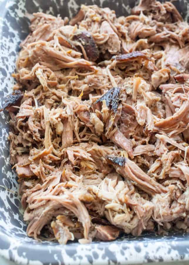Slow Cooker Pernil (Puerto Rican Pork Shoulder) | Over head view of a grey speckled casserole dish filled with shredded pork.