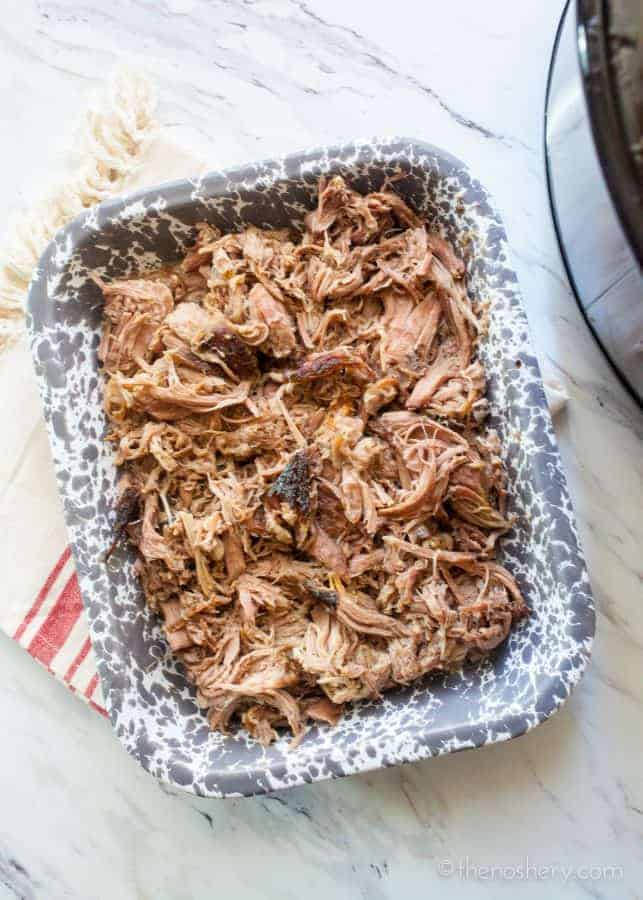 Slow Cooker Pernil (Puerto Rican Pork Shoulder) | Over head view of a grey speckled casserole dish filled with shredded pork.