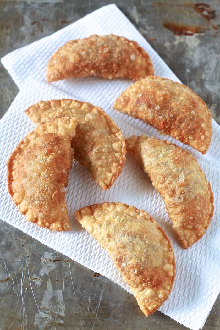 Pastelillos de Carne (Puerto Rican Meat Turnovers) with Homemade Pastelillo Dough Recipe| Fried pastelillos on paper towel on metal surface. | The Noshery