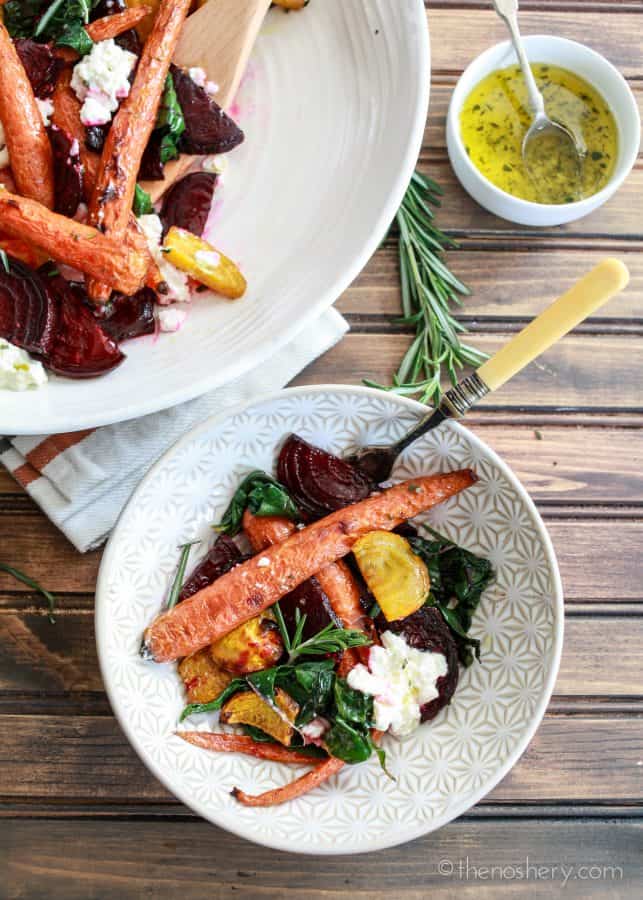 Roasted Beets and Carrots Salad with Burrata | Overhead view of bowl of roasted carrots, beets, beet greens, and burrata. Platter of salad in the background. With wood background. | The Noshery