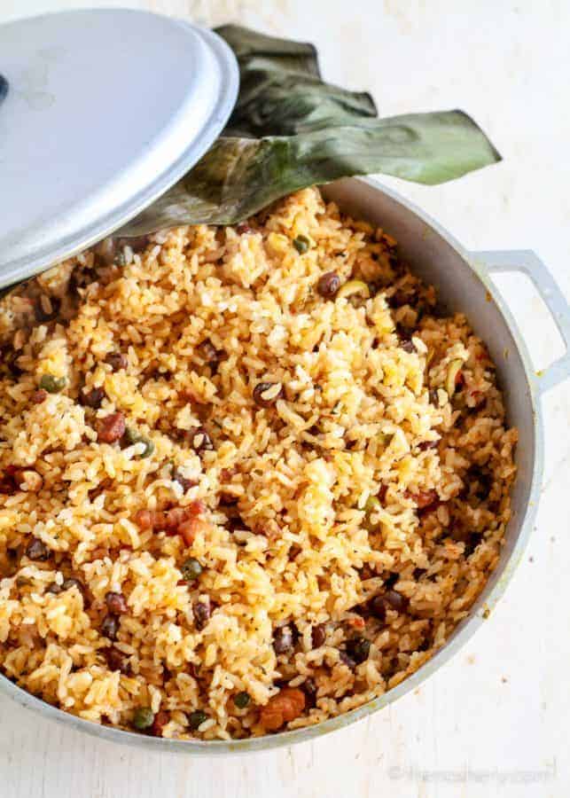 Arroz con Gandules (Puerto Rican Style Rice and Pigeon Peas) | Overhead view of large pot of orange colored rice with bacon and small dark green pigeon peas. 