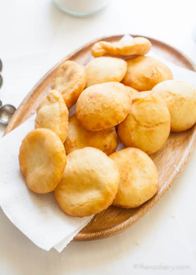 Arepas de Coco (Coconut Fry Bread) | Wood platter filled with round, golden, and puffy fry bread. | The Noshery