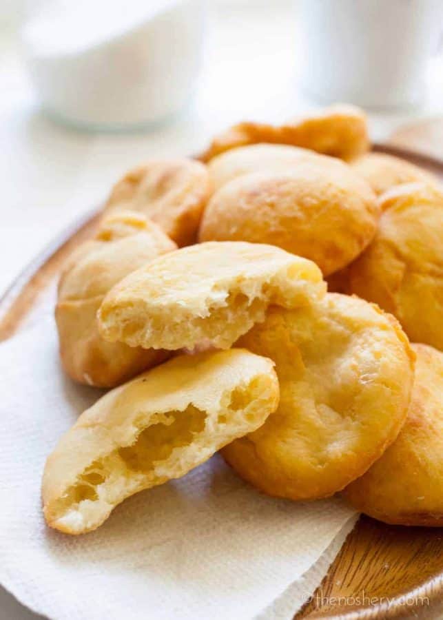 Arepas de Coco (Coconut Fry Bread) | Wood plate filled with golden puffy fry bread, with torn bread in foreground showing the air pocket inside. | TheNoshery.com