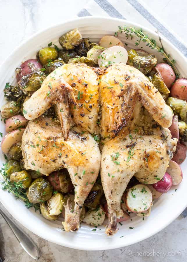 Lemon Garlic Spatchcock Chicken Dinner | Platter of whole spatchcock chicken on a bed of roasted Brussels sprouts and potatoes. | The Noshery
