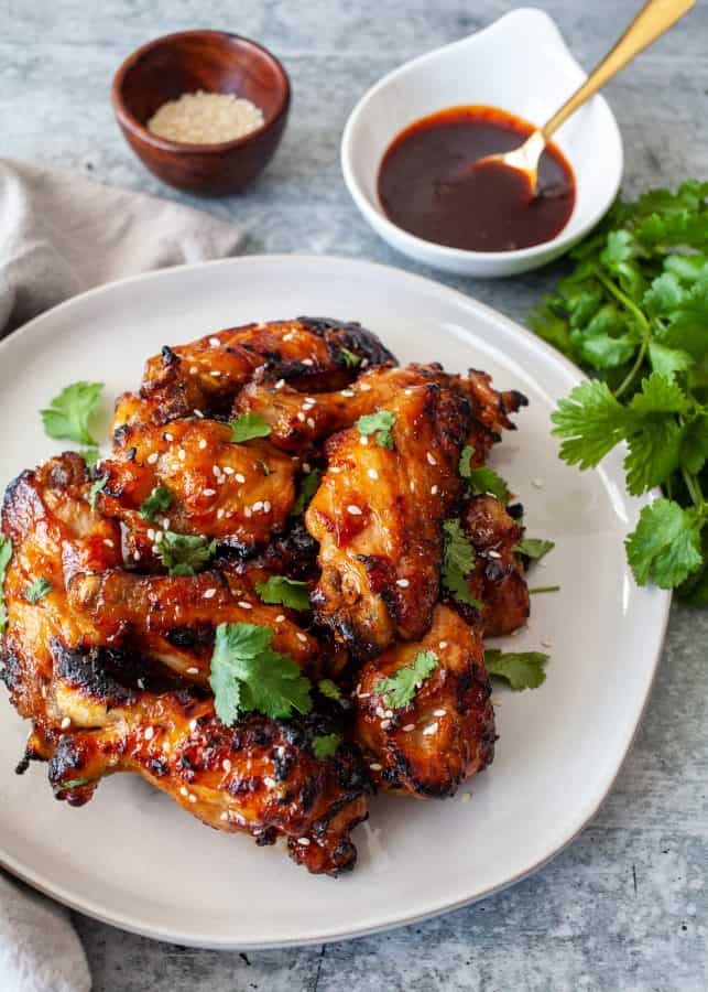 Instant Pot Sticky Gochujang Chicken Wings | Overhead shot of glazed chicken wings on a place with sauce in background. Wings are garnished with cilantro and sesame seeds.