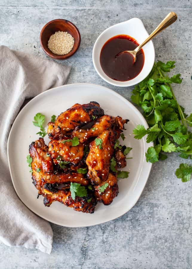 Instant Pot Sticky Gochujang Chicken Wings | Overhead shot of glazed chicken wings on a place with sauce in background. Wings are garnished with cilantro and sesame seeds.